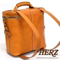 職人手作皮革大型三用旅行後背包，呈現自然棕色調，皮革材質，以白色縫線勾勒包身線條，設有頂部提把、拉鍊開口及兩條可調式肩帶，展現簡約實用的設計風格。