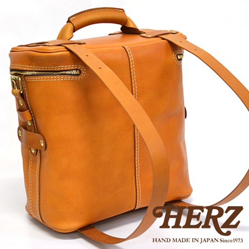 職人手作皮革大型三用旅行後背包，呈現自然棕色調，皮革材質，以白色縫線勾勒包身線條，設有頂部提把、拉鍊開口及兩條可調式肩帶，展現簡約實用的設計風格。