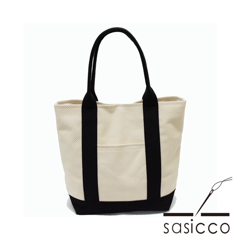 米白色三河木綿刺子織托特包，配有黑色提把和底部，正面有一個對稱的黑色口袋。