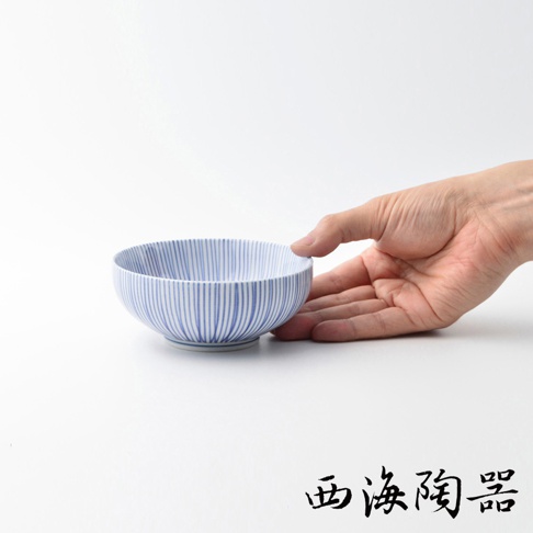 一個藍白相間、帶有細緻直條紋的波佐見燒小碗，碗身呈圓弧形，底部有淺色圈紋。一隻手捧著碗的右側，展示其尺寸。