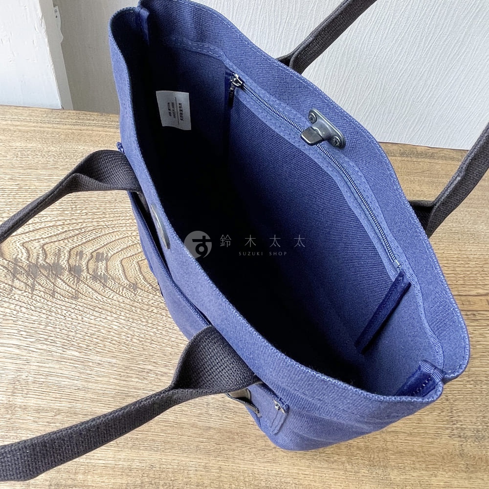 藍色帆布水桶托特包，內部有拉鍊隔層和品牌標籤，搭配深灰色提把。
