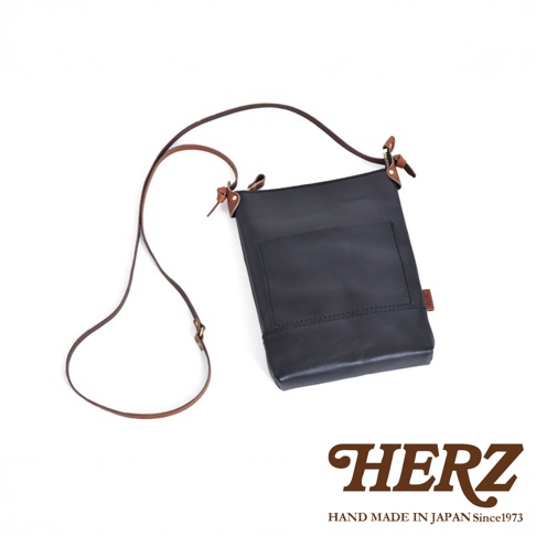 黑色皮革直式隨身單肩包，配有可調式棕色皮革背帶，包身有方形外袋。