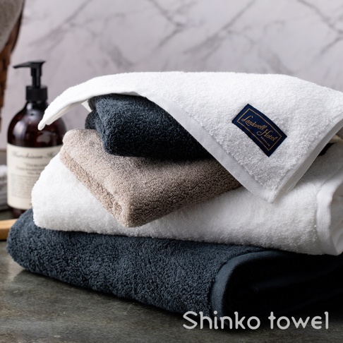 疊放的泉州匹馬棉浴巾，有深藍、淺棕和白色，其中白色浴巾上帶有藍色「Landwell Hotel」品牌標籤。