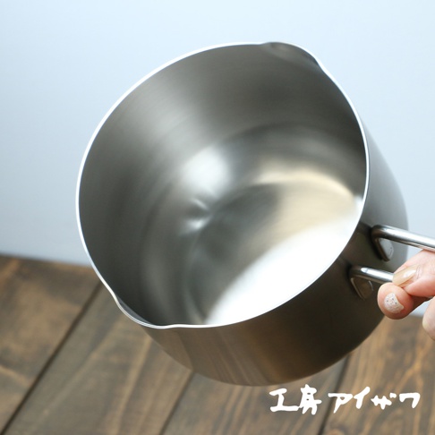 一個14公分的不鏽鋼雙口牛奶鍋，鍋身呈現銀色金屬光澤，設有兩個對稱的把手，鍋緣有方便傾倒的雙導流口設計。