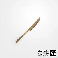 黃銅色起司刀，刀刃一側有鋸齒狀邊緣，刀柄圓潤，整體設計簡約，背景為純白色。