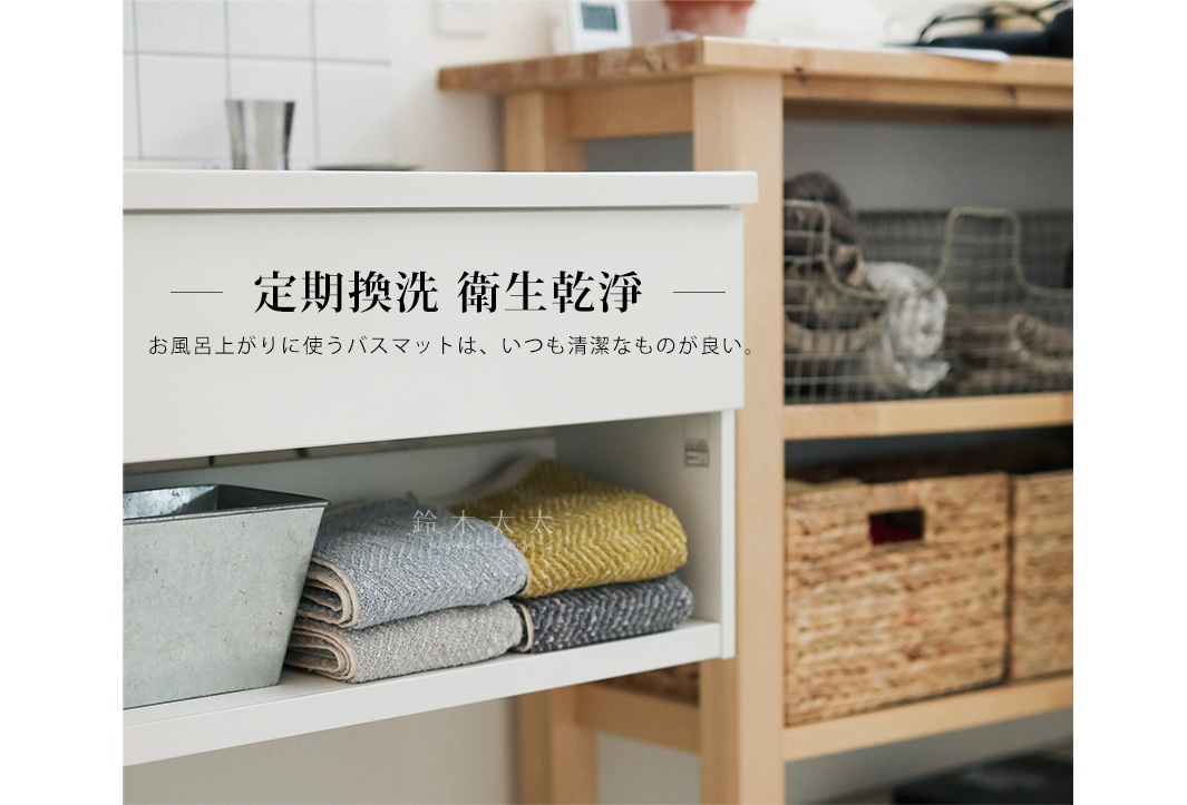 白色儲物櫃下方架子上，疊放著三條棉麻混紡人字紋浴巾，顏色分別為淺灰色、灰色和芥末黃。