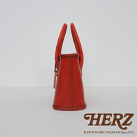 橘紅色皮革手提包，側面視角，有提把和縫線細節。