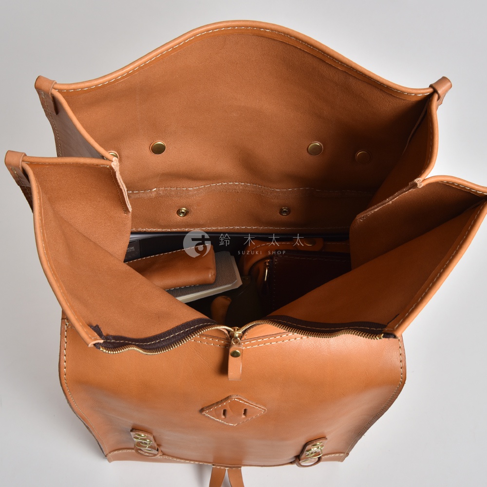 職人手作皮革後背包，顏色為棕褐色，材質為真皮。包款內部有分隔，可見筆記本、手機及零錢包等物品。包包正面有菱形縫線裝飾，並配有銅製金屬扣環及拉鍊。