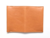 淺棕色皮革製成的翻蓋式記事本書套，表面光滑，邊緣有米白色縫線裝飾。