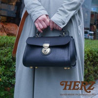 黑色皮革迷你手提包，配有金色鎖扣和四個金色底部鉚釘，由手工製作。