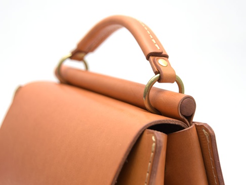 棕色皮革製成的兩用單肩包，帶有圓形提把和金屬環，細緻的縫線工藝。