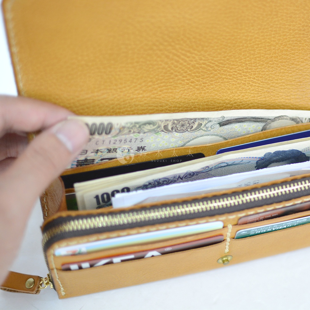 職人手作皮革長夾，展示內容物包含日圓鈔票、多張信用卡與證件。長夾為寬口設計，內部隔層可清楚收納各式卡片與鈔票。材質為質感皮革，顏色為溫暖的淺棕色。