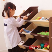 一個兒童正在操作一個多層玩具收納架，架子由深棕色木質框架和淺棕色及深棕色收納盒組成，收納盒內放有各式玩具，如積木、玩偶和球類。