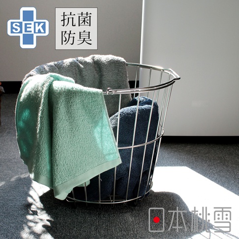 SEK抗菌防臭運動大毛巾，展示了淺綠色、海軍藍和灰色三種顏色。毛巾質地柔軟，堆疊在一個金屬絲籃子中，背景是白色家電和灰色地毯，有陽光灑落。