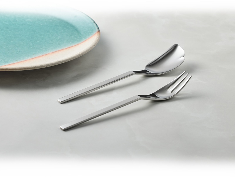 一組不鏽鋼蛋糕叉匙，叉子有三齒，湯匙形狀獨特，置於淺色背景上，旁邊有一塊藍綠色漸層的盤子。