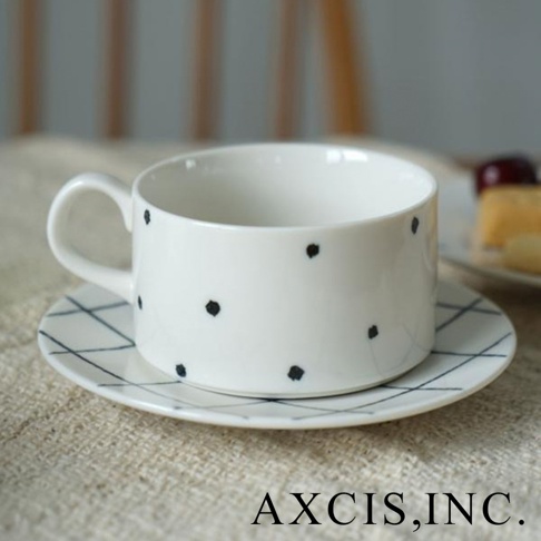 白色陶瓷咖啡杯，點綴著黑色手繪圓點，搭配同款白色陶瓷碟，碟面飾有黑色線條網格。
