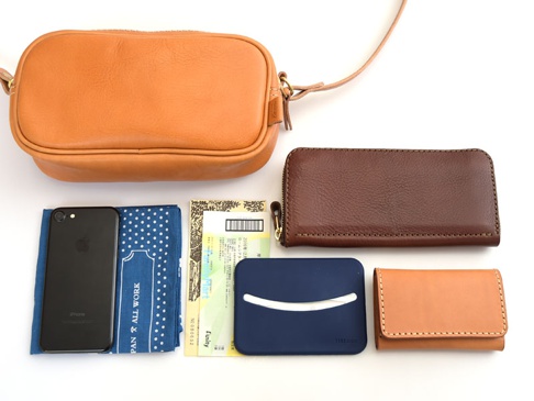 職人手作皮革隨身單肩小包 (CP-35)，搭配棕色皮革長夾、黑色手機、藍色印花布、黃色收據和藍色卡夾。
