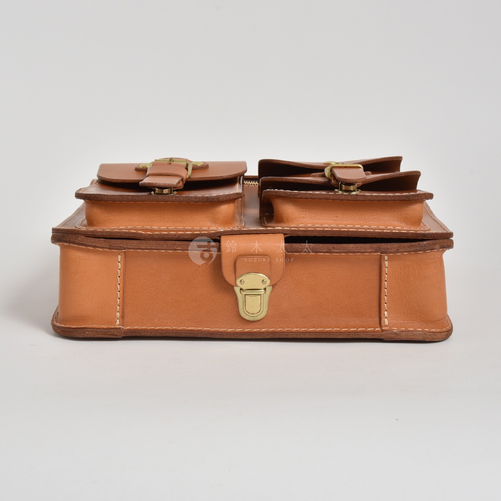 職人手作皮革三口袋三用後背包，採用天然皮革材質，呈現經典棕色調。包身設計有三個帶有銅釦皮帶的外部口袋，以及一個中央的鎖扣，展現精緻工藝。