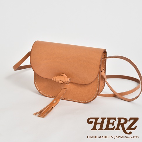 職人手作皮革流蘇側背包，採用天然皮革製成，呈現溫潤的淺棕色。包款設計簡約，以皮革繩結與流蘇為特色，展現手工質感。