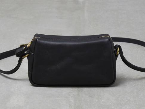 黑色皮革製成的職人手作輕巧拉鍊單肩包，配有金色拉鍊及金屬扣環，簡約設計，適合日常攜帶。