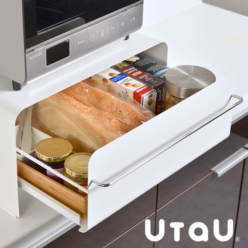 白色抽屜式收納櫃，內有兩條包裝吐司、數盒食品包裝、兩個果醬罐，以及一個玻璃罐。收納櫃側面有一個金屬拉柄，櫃體材質為金屬，內部有木製隔板。