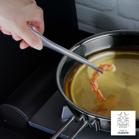 一只手正使用銀色金屬製的公筷夾，夾著一隻正在熱油中烹調的蝦。