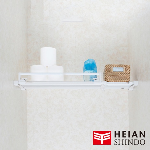 白色伸縮置物掛架上放置了三卷衛生紙、一個藍色塑膠瓶裝的清潔劑，以及一個編織籃，籃子裡有毛巾。