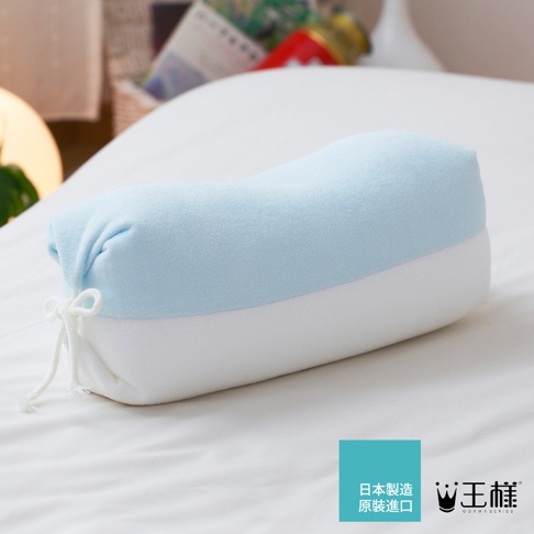日式糖果造型枕，上層為淺藍色絨布材質，下層為白色絨布材質，兩端以白色繩結固定，整體呈現圓柱形，擺放於白色床鋪上。