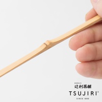 一雙手正拿著一根淺棕色、質地天然的竹製抹茶杓，杓柄上有明顯的竹節紋理。