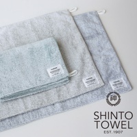 YUKINE 雪中漫步有機棉浴墊，展示了三種顏色：淺綠色、淺灰色和深灰色。浴墊由蓬鬆柔軟的有機棉製成，表面帶有細膩紋理。每塊浴墊上都有YUKINE品牌標籤，其中一塊還帶有「SHINTO TOWEL EST. 1907」的標誌。