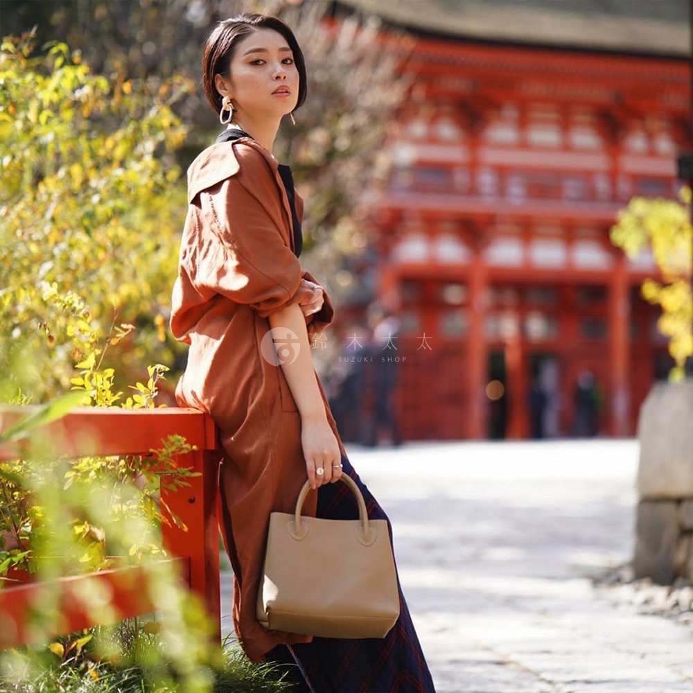 一位女士拿著一個淺棕色的皮革手提托特包，包包有兩個短手柄。