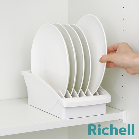 一個白色的餐盤收納架，裡面整齊擺放著五個白色圓形餐盤，一隻手正從右側取出其中一個餐盤。