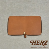 HERZ 品牌標誌，下方有 HAND MADE IN JAPAN Since1973 字樣，中間是一件棕色皮革製的拉鍊式收納包，置於灰色紋理背景上。