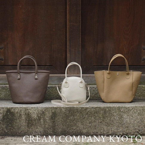 三款皮革手提包，分別為深棕色、米白色和淺棕色，皆為職人手作，設計簡潔，可在石階上展示。