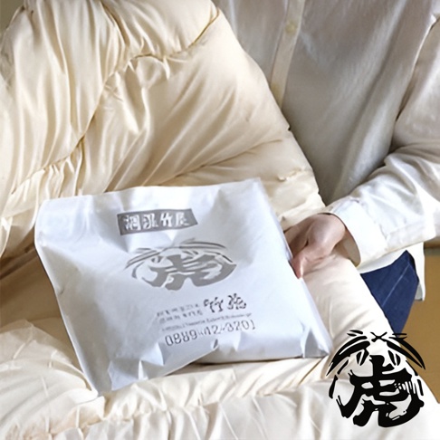 一包白色包裝的孟宗竹炭產品，上面印有中文「洞洞竹」、「竹炭」字樣及圖騰，包裝紙質，產品置於米白色蓬鬆織物上。