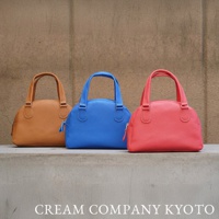 三款牛皮半月迷你手提包，分別為淺棕色、亮藍色及珊瑚紅色，皆帶有細緻的皮革紋理和圓潤的提把設計。