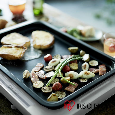 左右溫控電烤盤 WHP-012，黑色烤盤上烤著香腸、蘑菇、小番茄、洋蔥、蘆筍及吐司，盤子置於白色烤盤主體上，右下角有IRIS OHYAMA 品牌標誌。