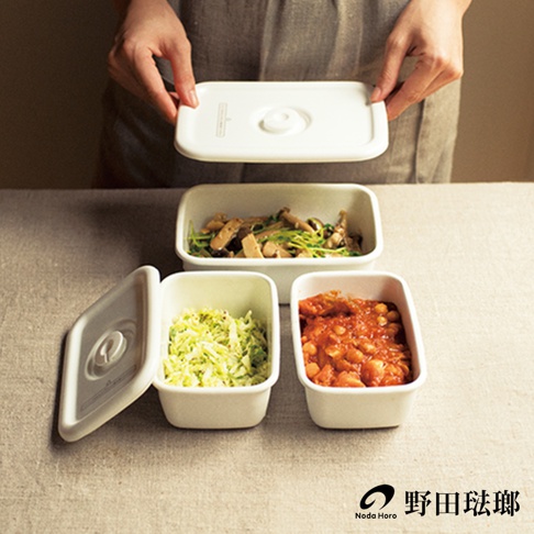 白色琺瑯長方型密封蓋保存容器，內含三種不同食物：炒菇、切絲蔬菜和番茄燉豆。其中一個容器的蓋子被打開，露出容器內的切絲蔬菜。