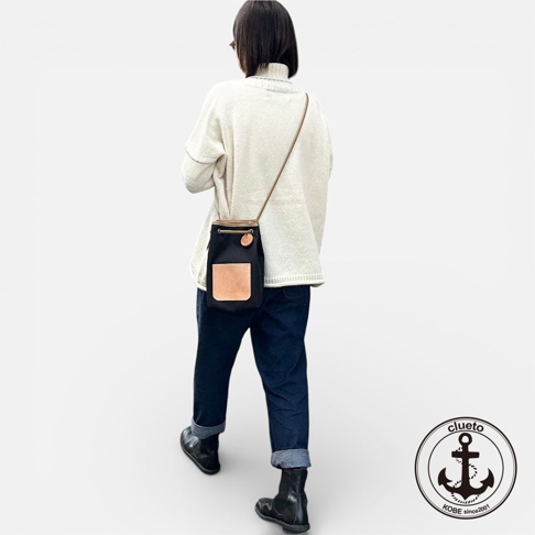 一位女子身穿白色高領毛衣與牛仔褲，斜背一個黑色束口袋小包，包上有義大利皮革口袋，她正走在有光影的白色背景前，右下角有clueto品牌標誌