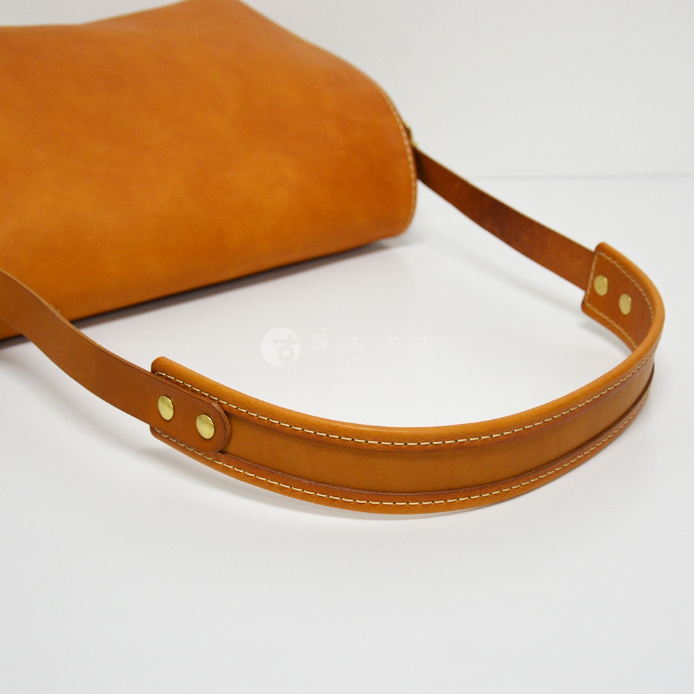 職人手作皮革復古翻蓋郵差包 CM-141，整體呈棕褐色，材質為真皮，包身呈現圓潤的曲線，搭配皮革提把，提把兩端以鉚釘固定，並有縫線裝飾。