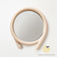 藤編圓鏡，鏡框由淺色天然藤條彎曲製成，形成獨特造型，底部藤條纏繞細節。