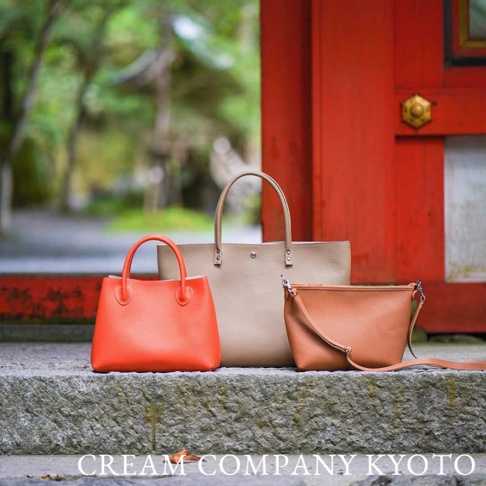 三款皮革手提包，分別為亮橘色、卡其色和棕色。亮橘色手提包造型簡約，配有提把。卡其色托特包較大，同樣有提把。棕色斜背包配有可調式斜背帶。