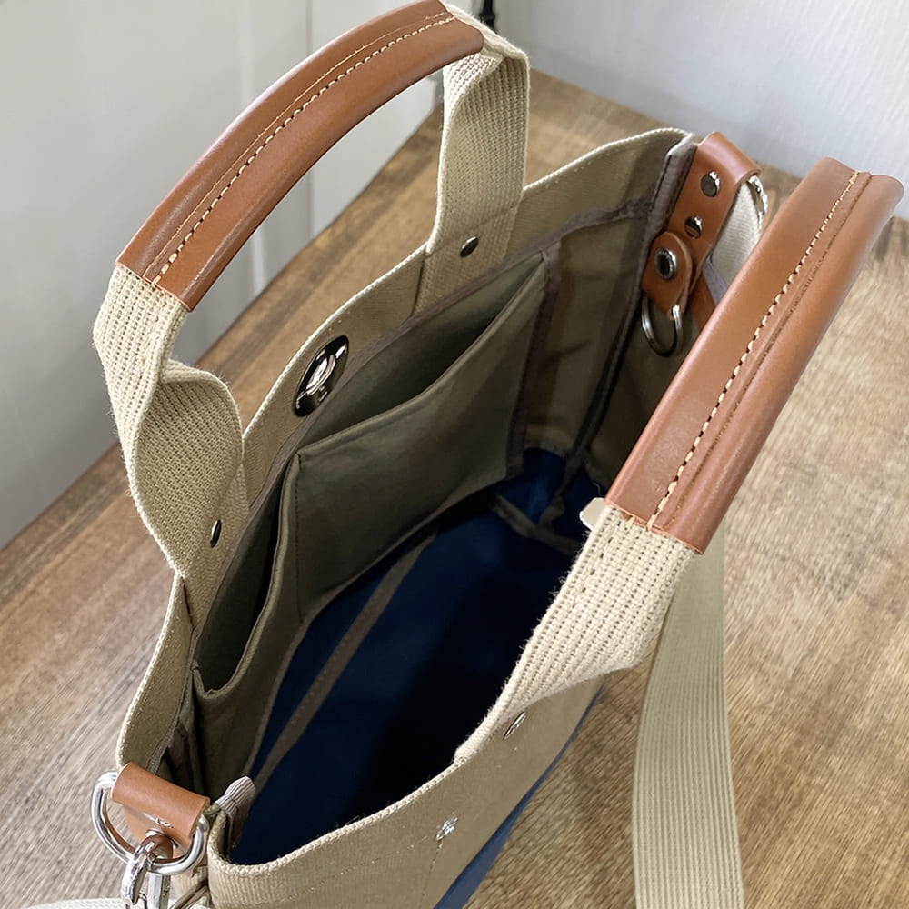 犬印純棉帆布兩用雙色托特包，帆布材質，米色外觀，內襯為深藍色條紋。提把為皮革材質，配有可拆卸肩帶。包內有多個隔層。