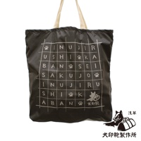 深灰色環保折疊收納購物袋，使用尼龍材質，袋身印有白色網格字母與腳印圖案，搭配米色織帶提把。