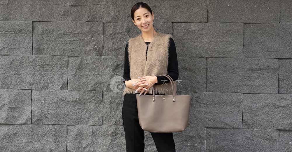 一位女性手持一個淺褐色皮革托特包，包的設計簡潔，有兩個肩帶。