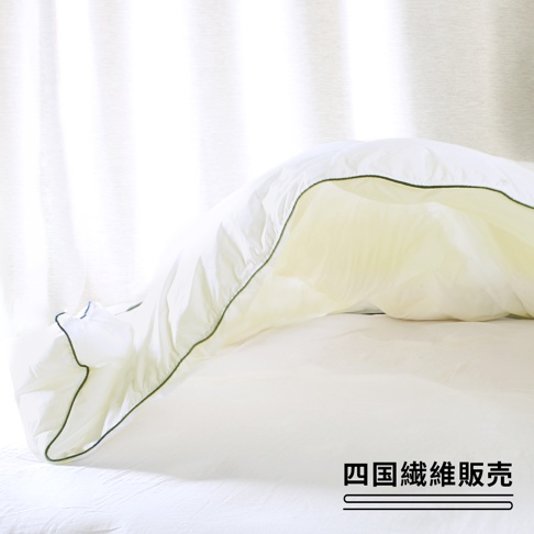 一張打開的雲絨被，被子為白色，邊緣有細緻的綠色滾邊，被子內部呈現淡黃色，整體鋪在白色的床單上，背景為白色窗簾。