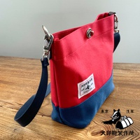犬印純綿帆布雙色迷你側背包，採用鮮紅色與海軍藍撞色設計，帆布材質，配有可調式背帶及金屬扣環，包身側面有品牌白色標籤。