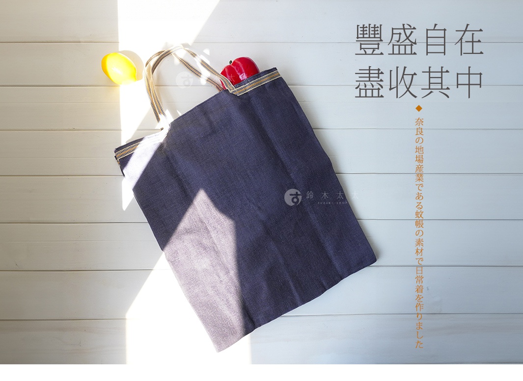 深藍色蚊帳棉織手提袋，配有米白色織紋提把，袋口有金屬拉鍊裝飾。袋身有日文品牌標誌。