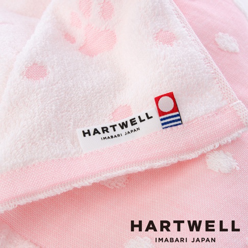 一條粉色與白色相間的今治純棉點點紗布浴巾，上面印有可愛的粉色小腳印圖案，並有 HARTWELL 品牌標籤。