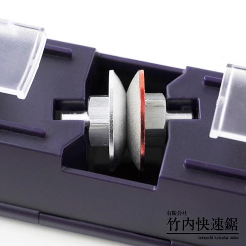 深紫色塑膠外殼內，兩個金屬軸上安裝著兩個圓形磨輪，一個為銀白色金屬材質，另一個為帶有紅色邊緣的磨輪，兩者之間有空隙。
